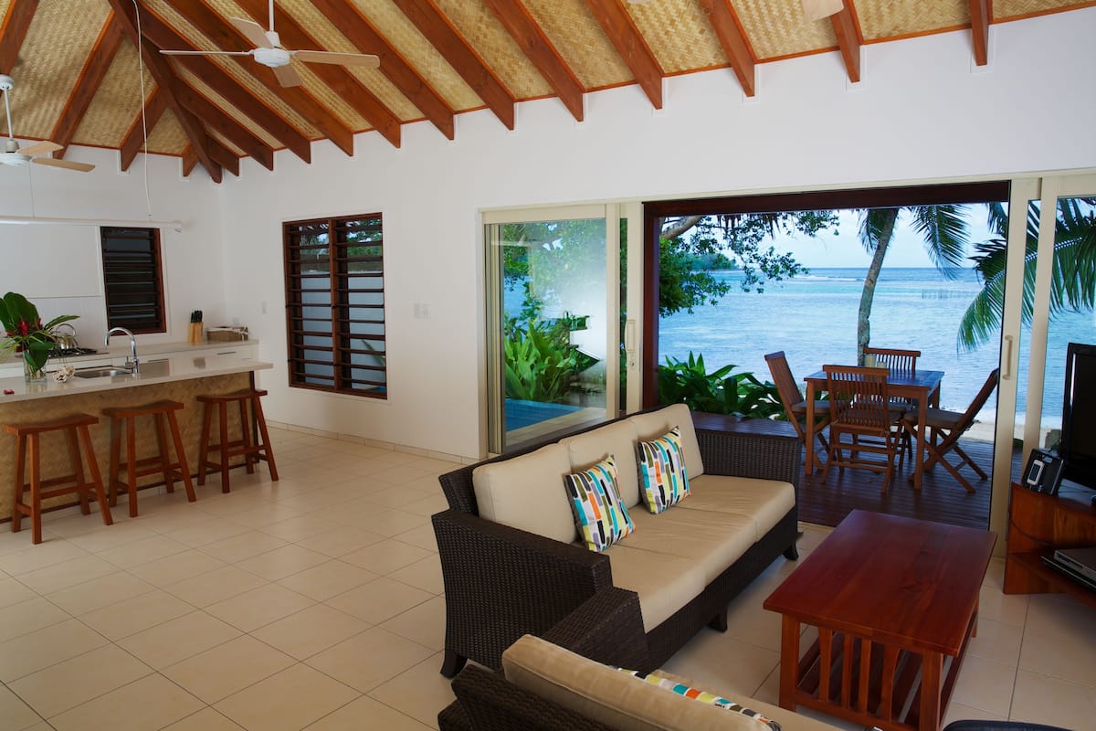 A spacious living area with a sofa, a wooden table, and a kitchen area with a bar counter and stools.