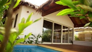 Una casa moderna con piscina, puertas correderas de cristal grandes y techo de paja.