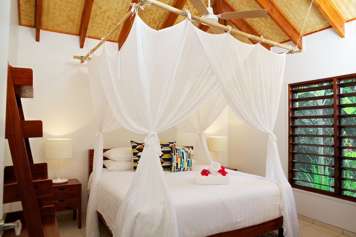 A bedroom with a four-poster bed, a wooden nightstand, a bedside table, and a window with blinds.