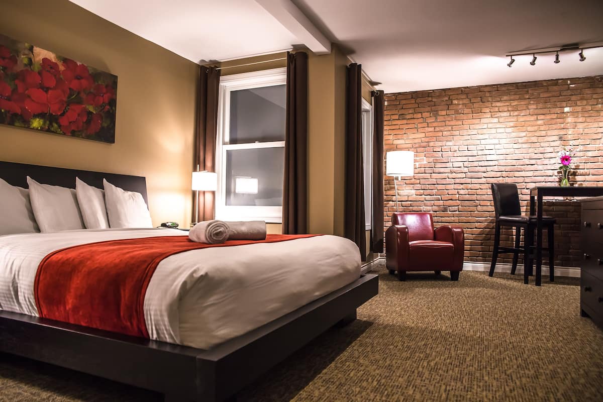 A hotel room with a large bed, a desk with a chair, a brick wall, and a painting of flowers.