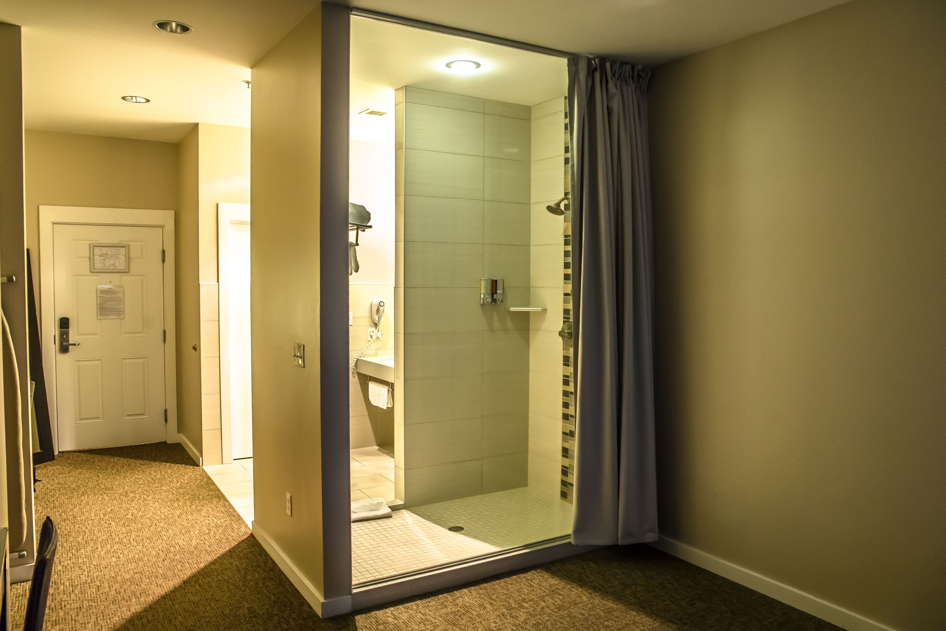 Un baño de hotel con cabina de ducha de vidrio, una puerta blanca y un área de lavamanos visible.