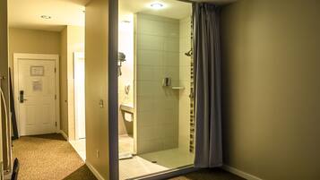 A hotel bathroom with a glass shower enclosure, a white door, and a visible sink area.