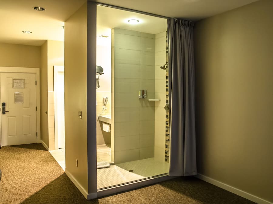 A hotel bathroom with a glass shower enclosure, a white door, and a visible sink area.