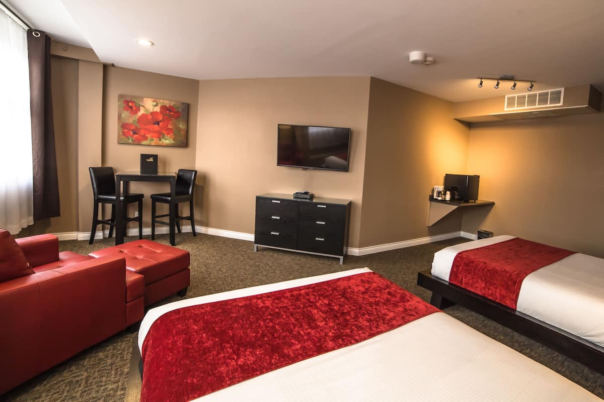 A hotel room with two beds, a red sofa, a desk with a chair, a TV, and a coffee machine.