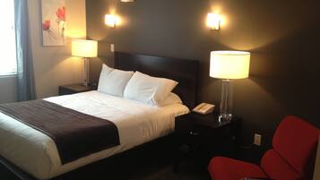 Habitación de hotel con cama, dos lámparas de noche, mesita de noche con teléfono, una silla roja y aire acondicionado instalado en la pared.