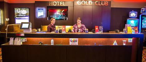 A hotel reception desk with a digital screen displaying the hotel name, a sign for the Gold Club, and a sign offering monthly birthday gifts.