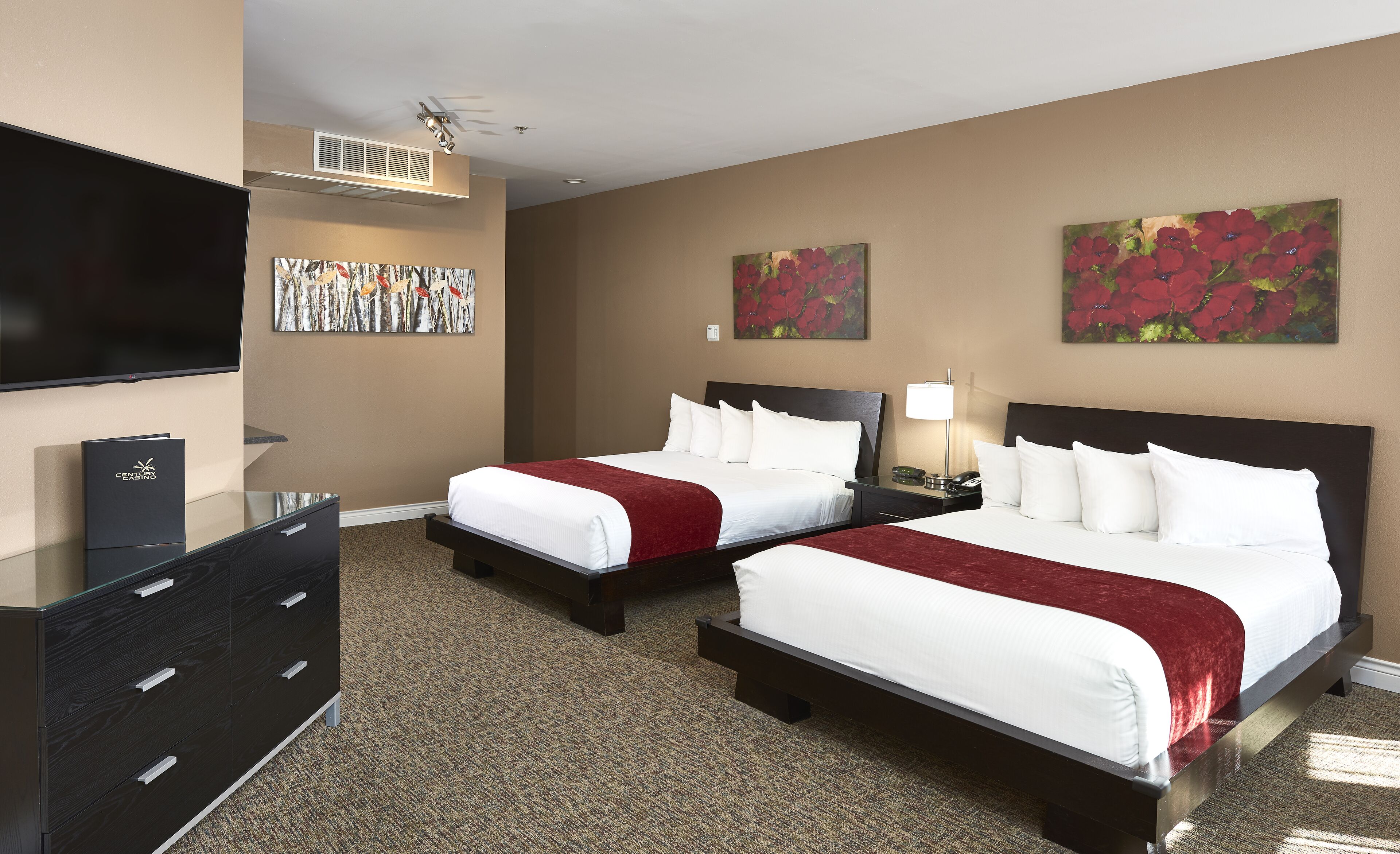 A hotel room with two beds, a flat-screen TV, a dresser, and artwork on the walls.
