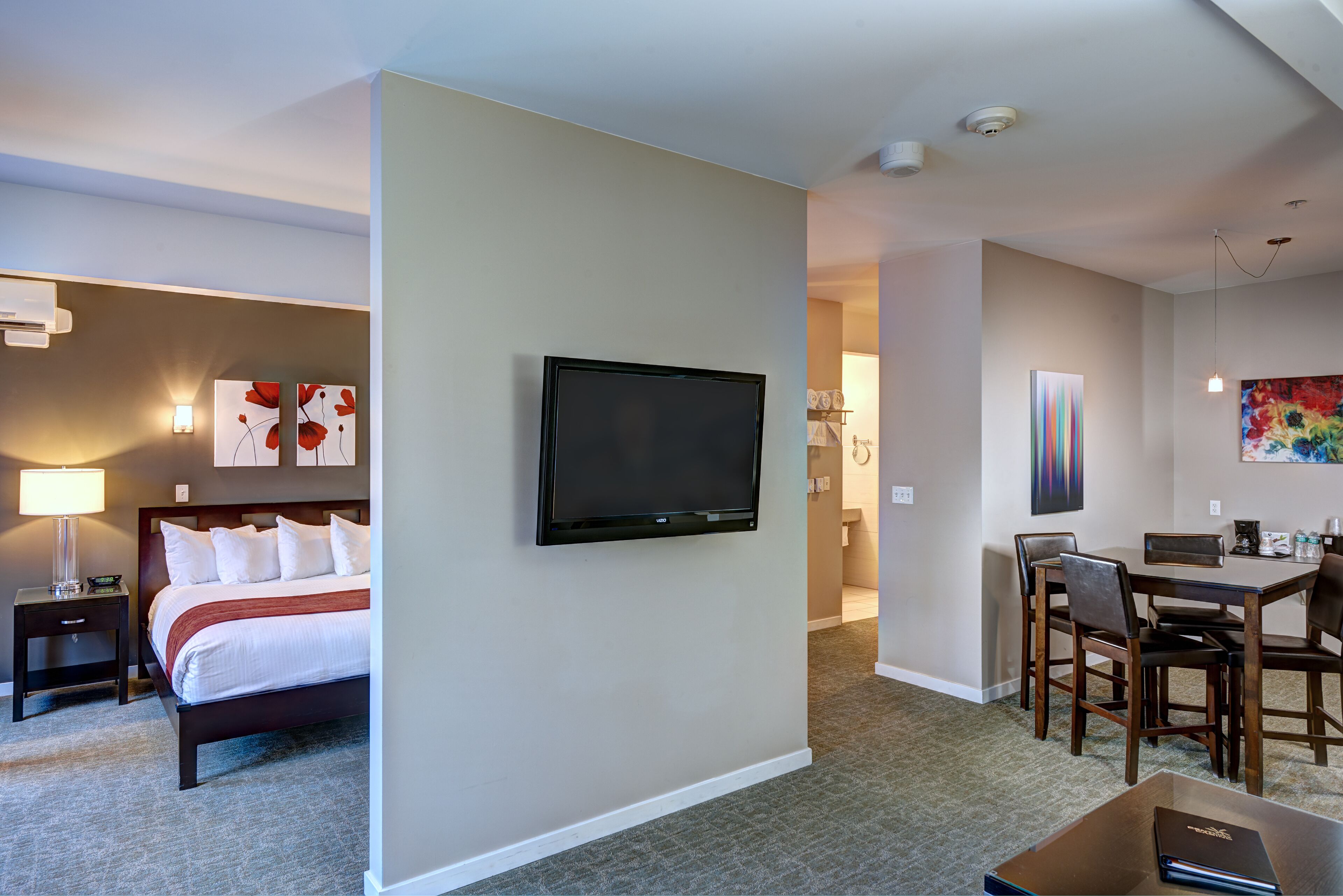 A hotel room with a bed, bedside table, lamp, TV, and a dining area with chairs and a table.
