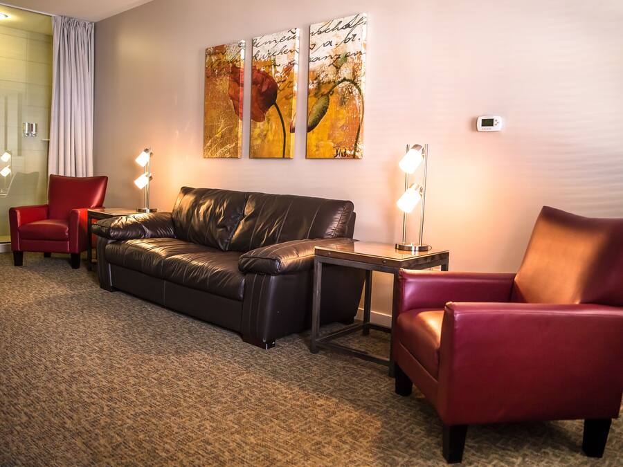 A hotel room with a leather sofa, two red armchairs, a small table, and a wall-mounted artwork.
