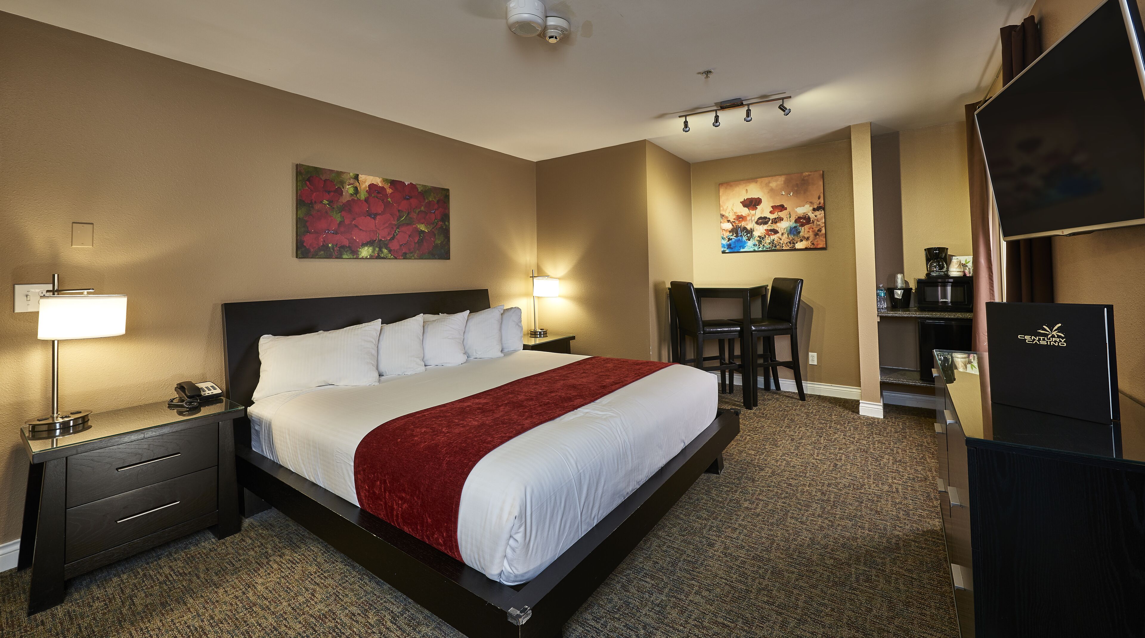 A hotel room with a large bed, bedside tables with lamps, a desk with a chair, and artwork on the walls.