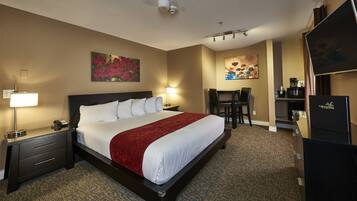 A hotel room with a large bed, bedside tables with lamps, a desk with a chair, and artwork on the walls.