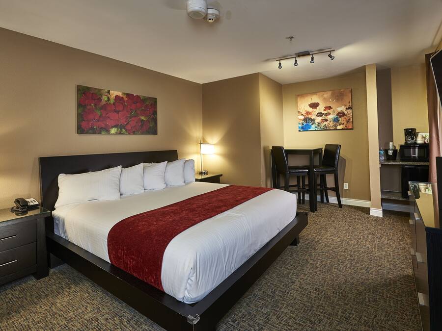 A hotel room with a large bed, bedside tables with lamps, a desk with a chair, and artwork on the walls.
