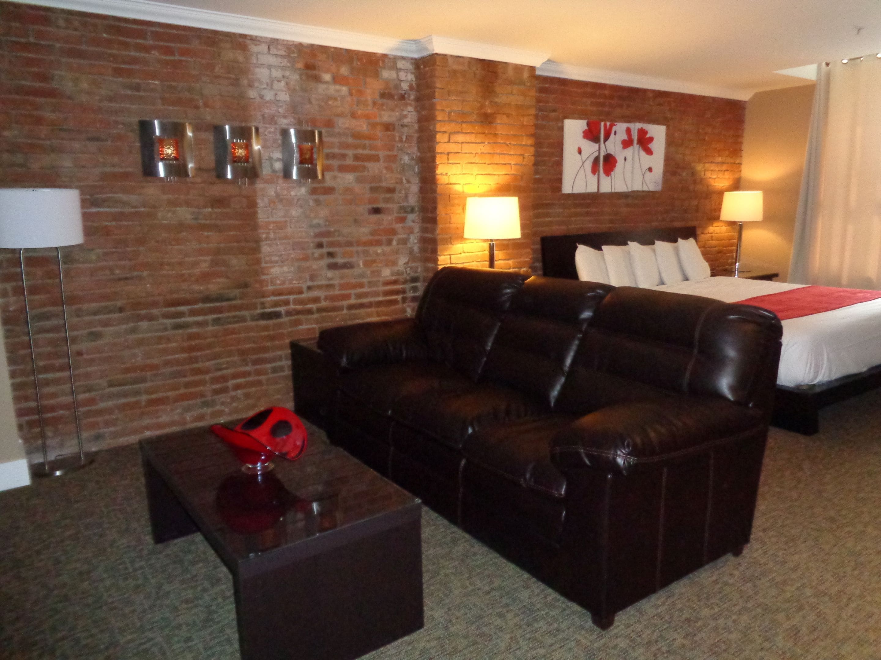 A hotel room with a brick wall, a leather sofa, a bed with white bedding, and two lamps.