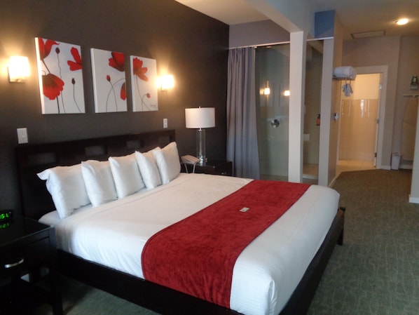 A hotel room with a large bed, a nightstand, a lamp, and artwork on the wall.