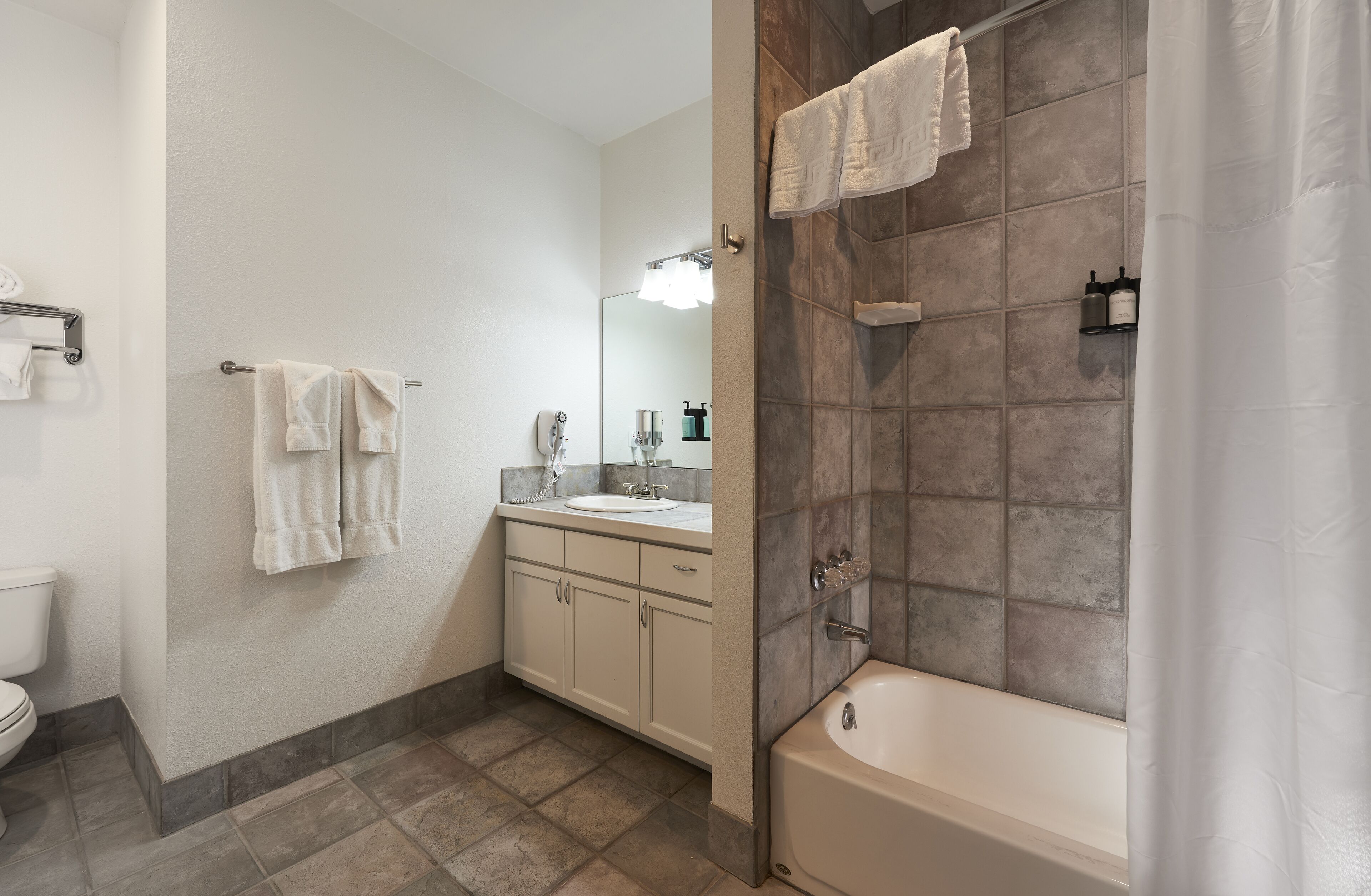 A modern bathroom with a bathtub, a sink, and a toilet. There are towels hanging on a rack and a mirror above the sink.