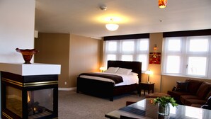 A bedroom with a bed, bedside lamps, a fireplace, a sofa, and a dining table.