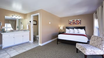 A hotel room with a large bed, a sitting area, a bathroom with a vanity, and a painting on the wall.