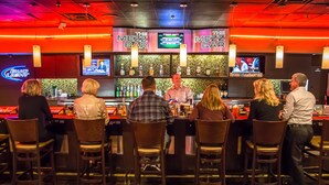 A bar with multiple screens and a counter where a bartender is serving drinks.