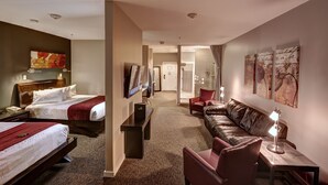 A hotel room with two beds, a sitting area with a leather sofa, a small table, and a TV.