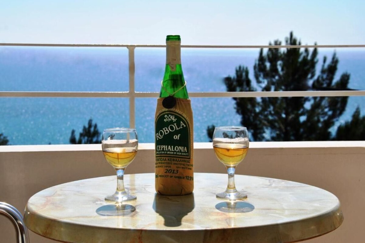 A bottle of Robola of Cephalonia wine and two glasses on a table with a view of the sea.