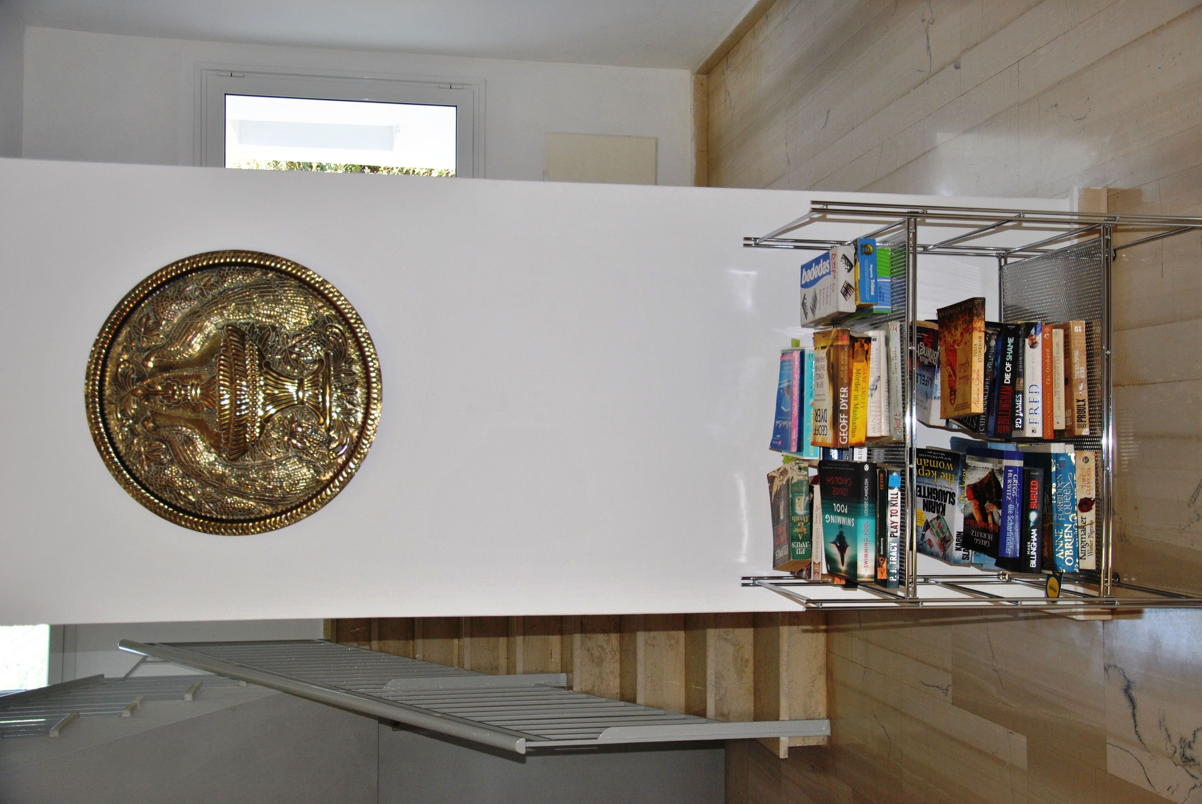 A room with a white wall, a large decorative emblem, and a metal shelf with books.