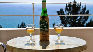 A bottle of Robola Cephalonia wine on a table with two glasses of wine, set against a scenic ocean view. - Filoxenia Hotel & Apartments (Kefalonia)
