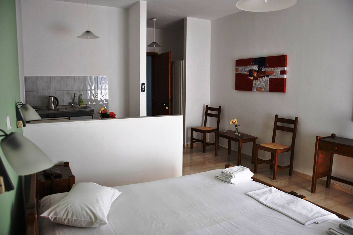 A hotel room with a bed, a desk, a chair, a small table, and a kitchenette.