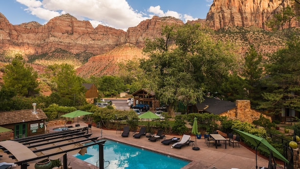 A pool area with lounge chairs and umbrellas, surrounded by greenery and a mountainous backdrop. - Flanigan's Resort and Spa (Springdale)