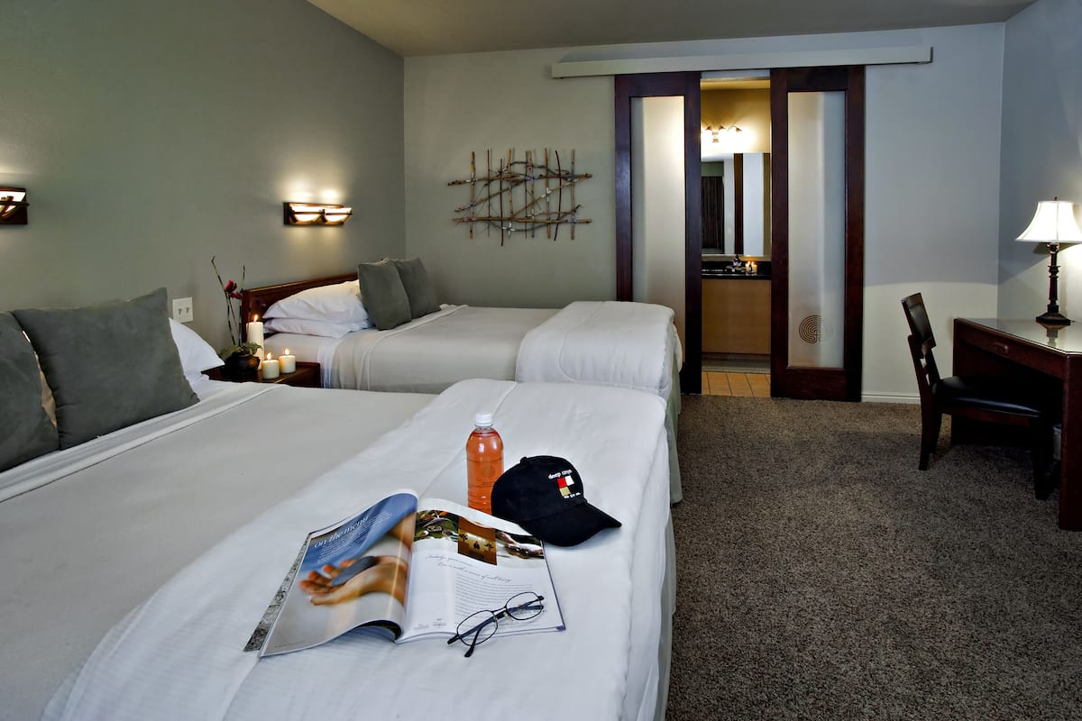 Een hotelkamer met twee bedden, een bureau, een stoel en een nachtkastje met een lamp.