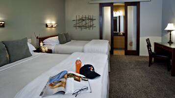 A hotel room with two beds, a desk, a chair, and a nightstand with a lamp.
