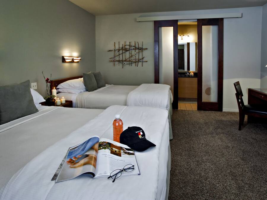 A hotel room with two beds, a desk, a chair, and a nightstand with a lamp.