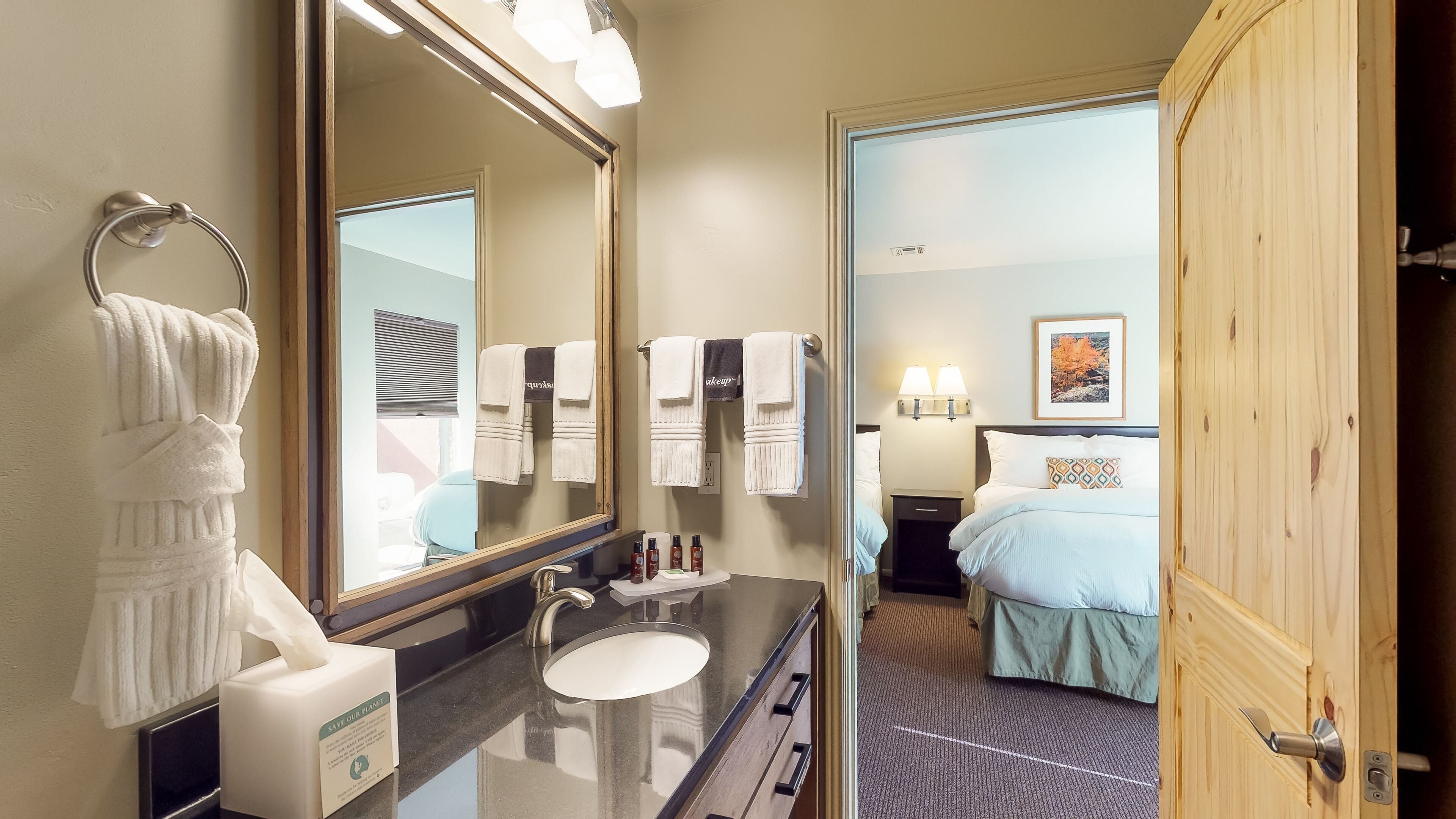A hotel bathroom with a large mirror, a sink, and a towel rack.