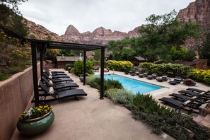 A pool area with lounge chairs and a pergola, surrounded by greenery and mountains in the background.