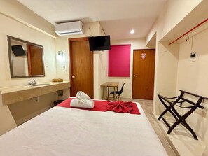 A hotel room with a bed, a desk, a chair, a TV, a bathroom with a mirror, and an air conditioning unit. - Hotel Barranquilla (Campeche)