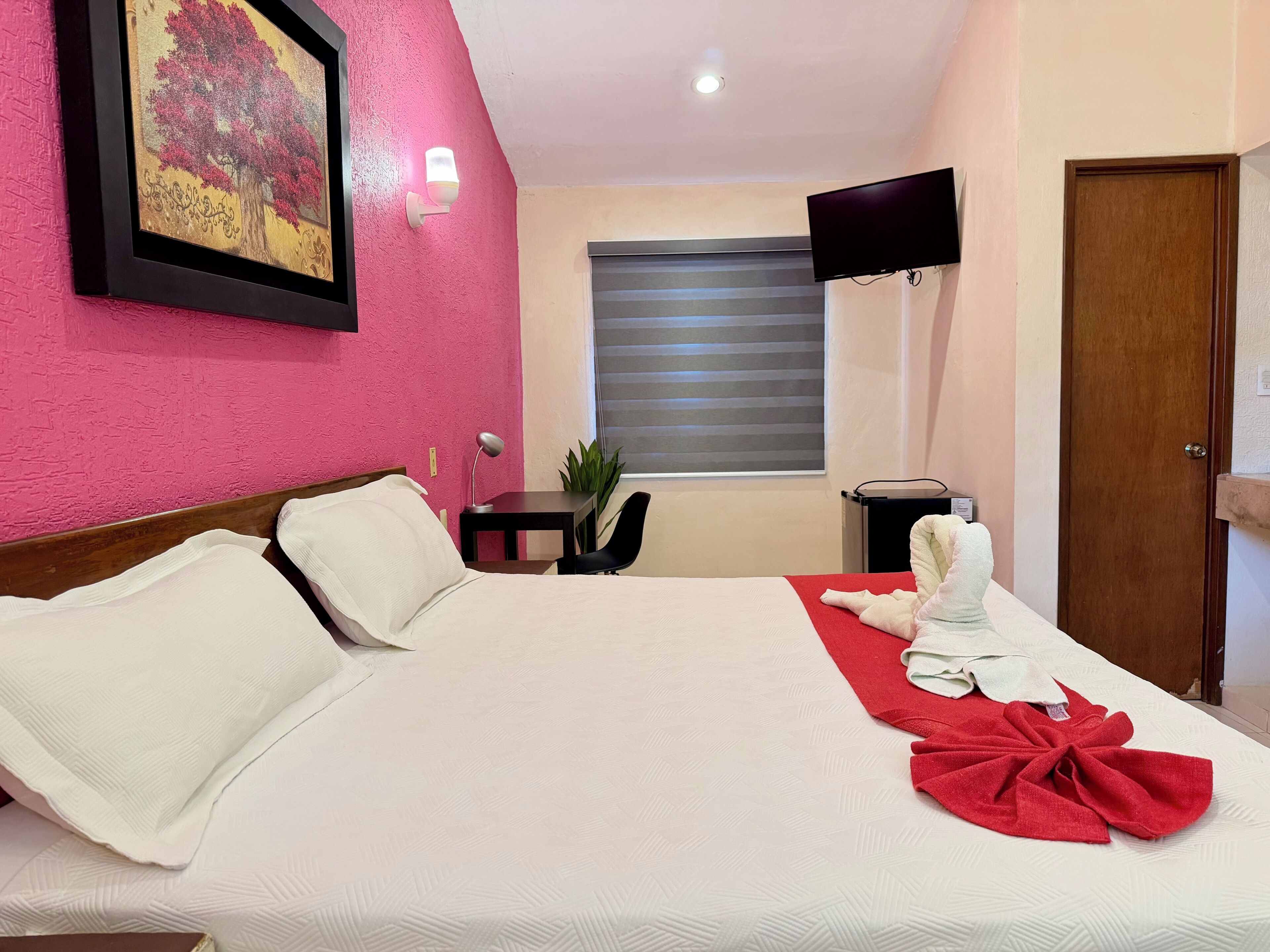 Habitación de hotel con cama, escritorio, silla, televisor y puerta.