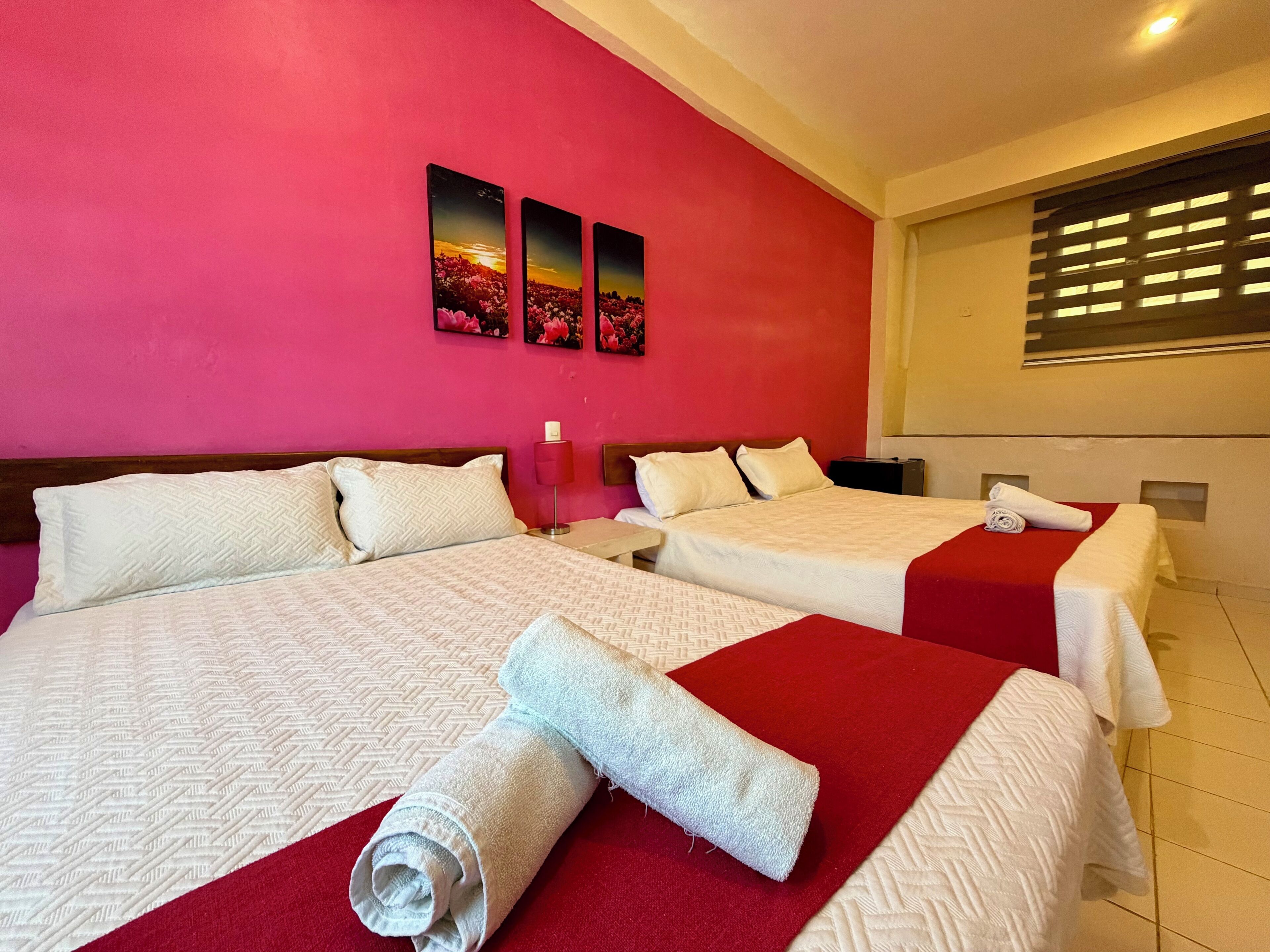 Quarto de hotel com duas camas, uma parede vermelha e uma janela com persianas.