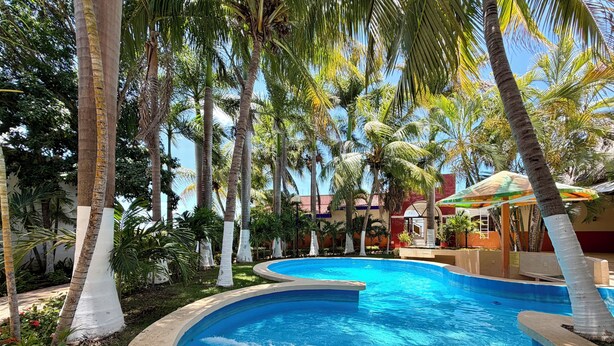 A swimming pool surrounded by palm trees and a building with a red and white facade. - Hotel Barranquilla (Campeche)
