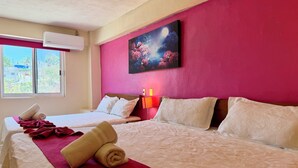 A hotel room with two beds, a large window, an air conditioner, a painting, and a nightstand with a lamp. - Hotel Barranquilla (Campeche)
