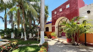 A courtyard with palm trees, a pool, and a building with red and white walls. - Hotel Barranquilla (Campeche)
