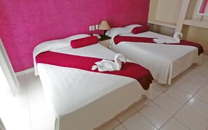 Two beds with white and red bedding, a lamp on the nightstand, and a pink wall.