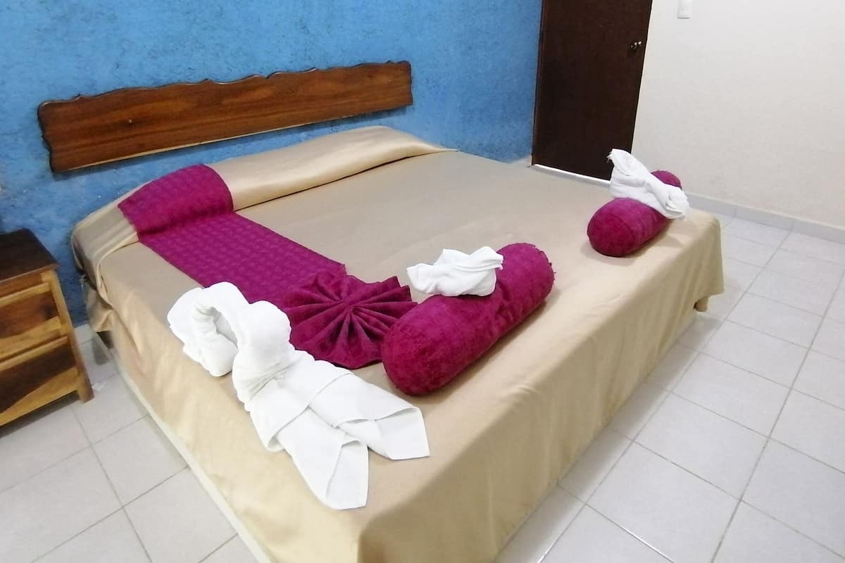A neatly made bed with a beige bedspread, pink and white towels, and a wooden headboard.