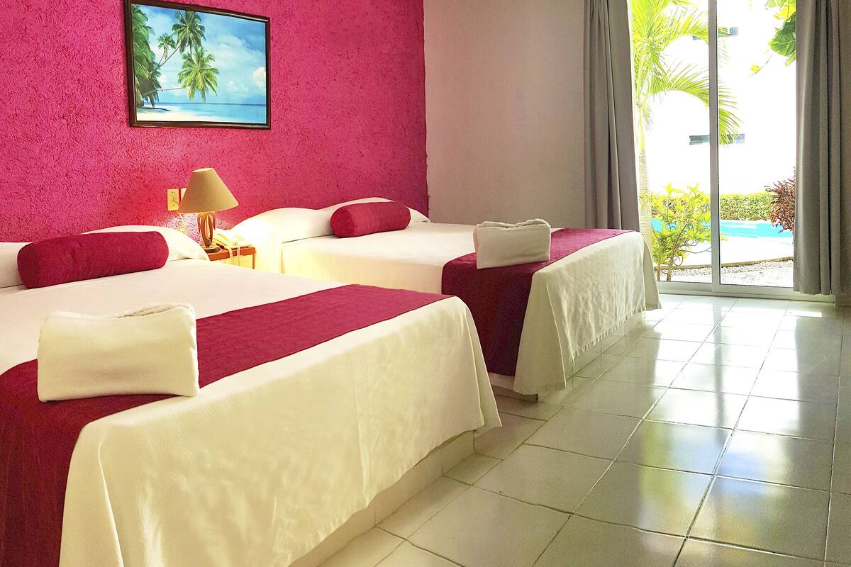 A hotel room with two beds, a painting of a beach scene, and a view of a pool through the window.