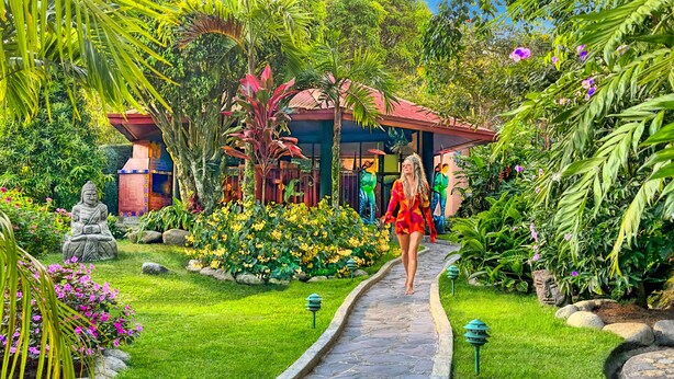 A garden with a Buddha statue, a colorful building, and a pathway.