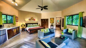 A spacious room with a bed, two sofas, a small table, a TV, and a ceiling fan.
