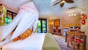 A bedroom with a canopy bed, a dining area with wooden chairs, a kitchen area with a microwave, and a ceiling fan.