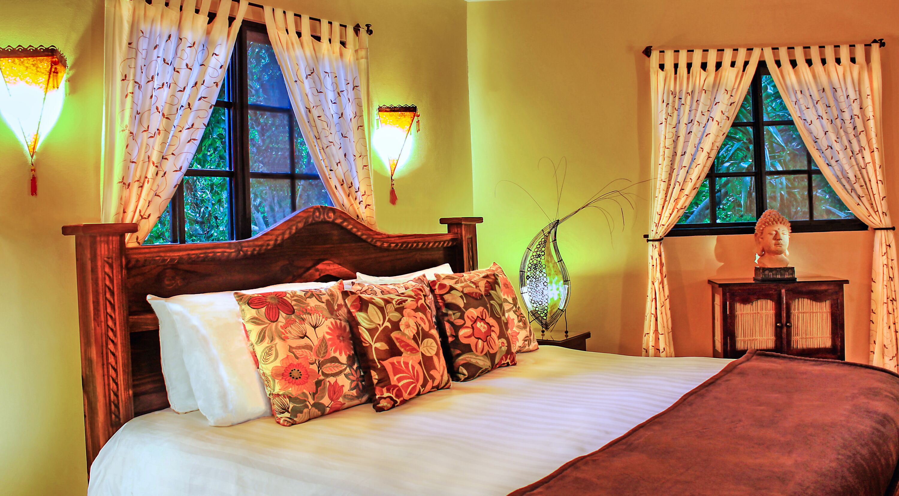A bed with floral bedding, a wooden headboard, and two wall-mounted lamps.