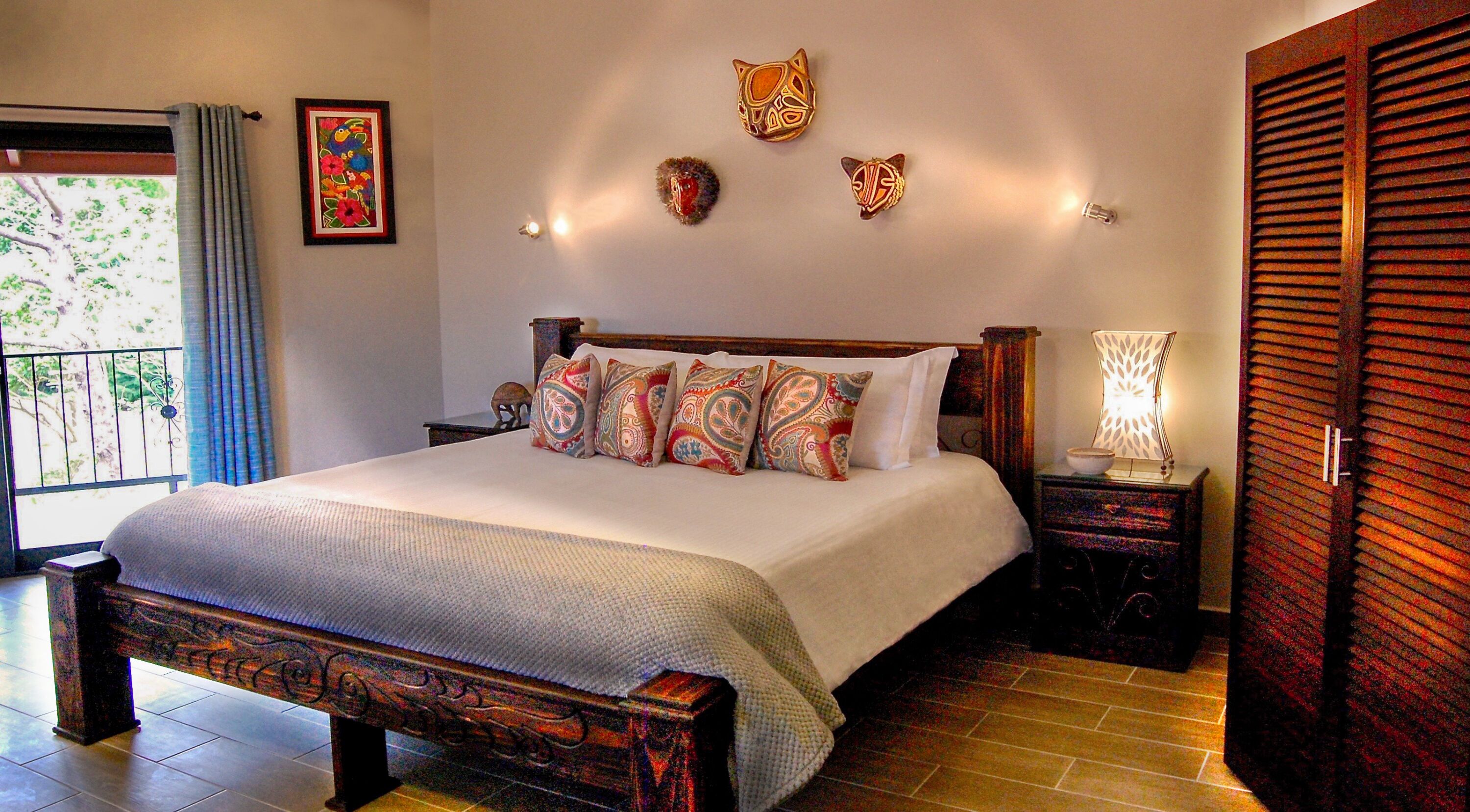 Un dormitorio con una cama grande, almohadas estampadas, una mesita de noche con lámpara y un armario de madera.