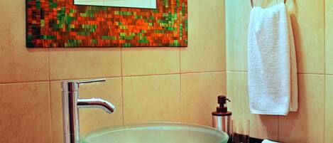 A bathroom with a glass bowl sink, a chrome faucet, a soap dispenser, and a towel hanging on a rack.