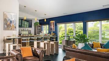 A modern living room with leather sofas, a bar area, and large windows offering a view of greenery.