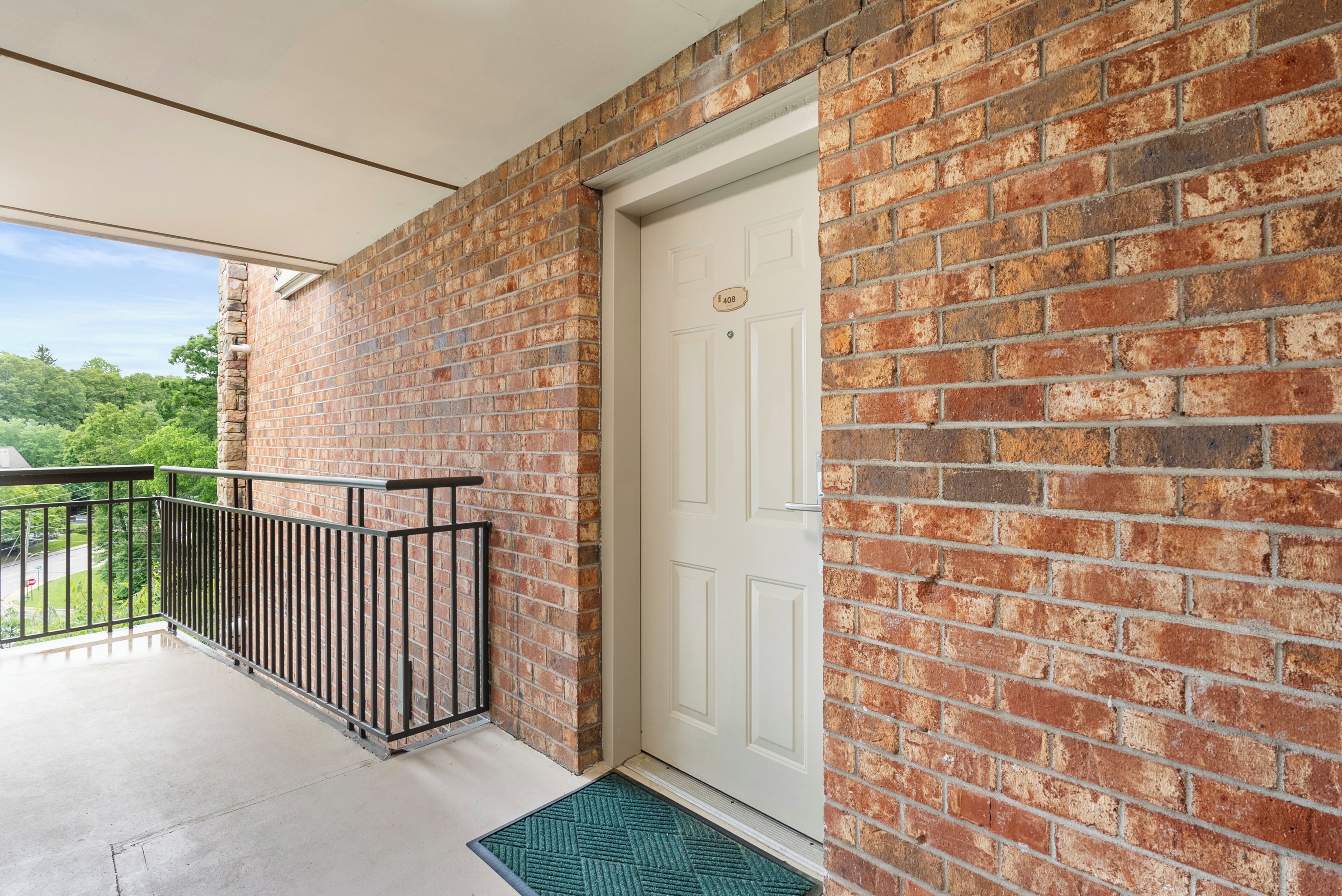 A balcony with a metal railing, a white door, and a brick wall.
